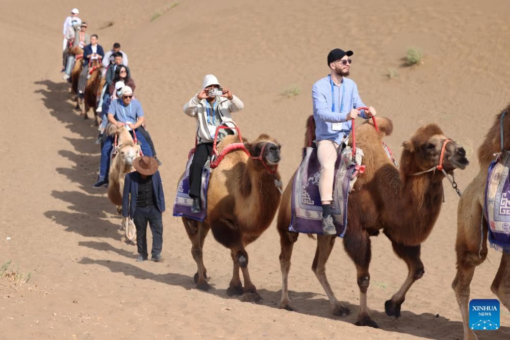Attendees of the 6th World Media Summit experience camel riding at a desert in Turpan, northwest China's Xinjiang Uygur Autonomous Region, Oct. 16, 2024.