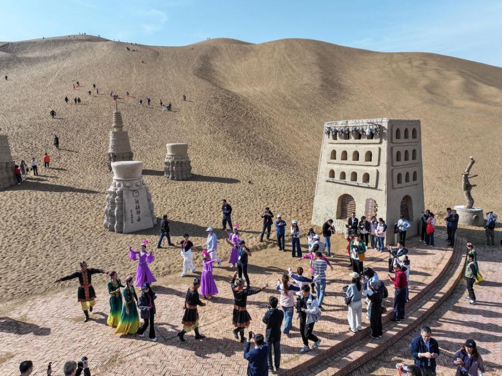 A drone photo taken on Oct. 16, 2024 shows attendees of the 6th World Media Summit dancing with performers at a desert in Turpan, northwest China's Xinjiang Uygur Autonomous Region. The 6th World Media Summit opened on Monday in Urumqi, capital city of Xinjiang. Attendees of the Summit would visit various places of Xinjiang during the Summit period. (Xinhua/Chen Yehua)