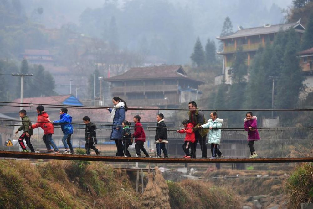 Zheng Changhao (3nd R), a local poverty alleviation official, leads children with his wife Wu Han (5th L) on a bridge in Wuying Village on the border between south China's Guangxi Zhuang Autonomous Region and southwest China's Guizhou Province, Jan. 30, 2021. (Xinhua/Huang Xiaobang)