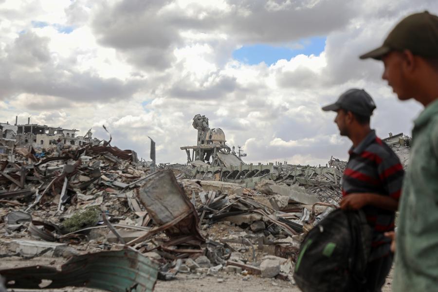 Palestinians walk past the rubble of destroyed buildings after returning to Khan Younis, in southern Gaza Strip, on October 12, 2025.