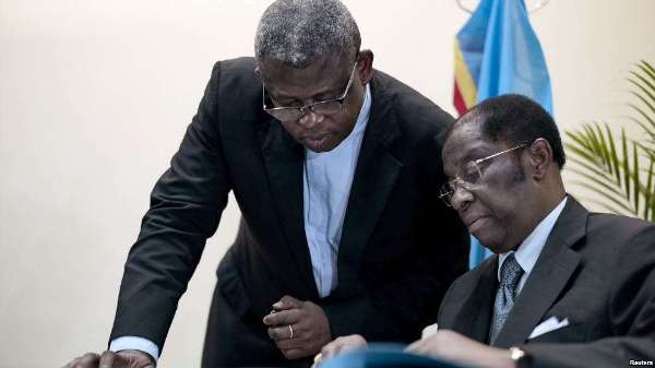 Congolese Justice Minister Alexis Thambwe Mwamba, right, is assisted by Abbot Donatiuen N'shole, CENCO secretary general, as he signs the accord between the opposition and the government of President Joseph Kabila at CENCO headquarters in Kinshasa, Dec. 31, 2016.