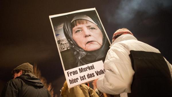 An anti-Islam Pegida activist holds a picture of Merkel in a headscarf with the words 'Mrs Merkel - here is the people'
