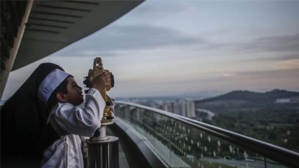 A mother holds her son to look at a theodolite to determine the sighting of the new moon to mark the start of Ramadan