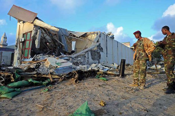 Somali soldiers and resident stand near the wreckage on February,27, 2016 in Mogadishu, Somalia At least 14 people were killed on February 26 as twin blasts and gunfire rocked a hotel.