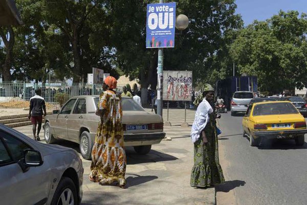 People walk by a banner reading " I vote Yes" as they go about with their daily life in Thies on March 16, 2016 on the second to last day of the political campaign on constitutional reforms including the reduction of the presidential mandate, a referenda looking more like a vote in favour or not of Senegal's President Macky Sall.