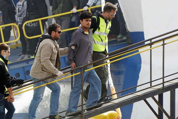 Frontex officials escort a migrant aboard a Turkish boat heading to Turkey on April 8, 2016 in the port of Mytilene on the Greek island of Lesbos. Greece deported a second batch of more than 100 migrants to Turkey while Germany announced a sharp drop in asylum claims as Europe toughens efforts to end its worst migration crisis since World War II.