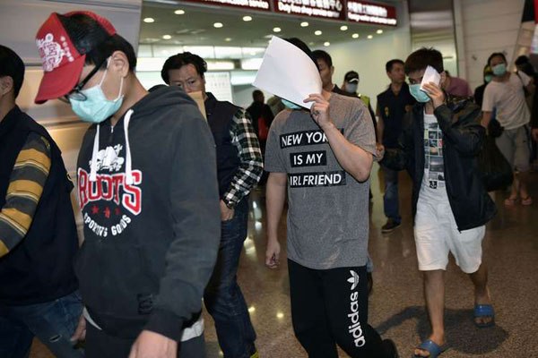 Masked alleged fraud suspects are escorted by unseen policemen as they arrive at Taoyuan Airport in Taoyuan on April 15, 2016.