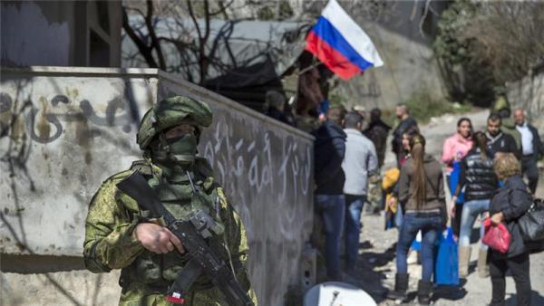 A Russian soldier stands guard as Syrians receive aid in the village of Ghunaymiyah