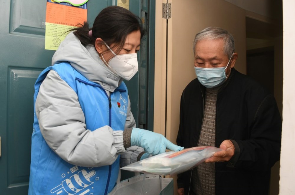 A community worker (L) explains a COVID-19 prevention and care package to a resident in Yangfangdian Subdistrict of Haidian District in Beijing, capital of China, Dec. 27, 2022. (Xinhua/Ren Chao)