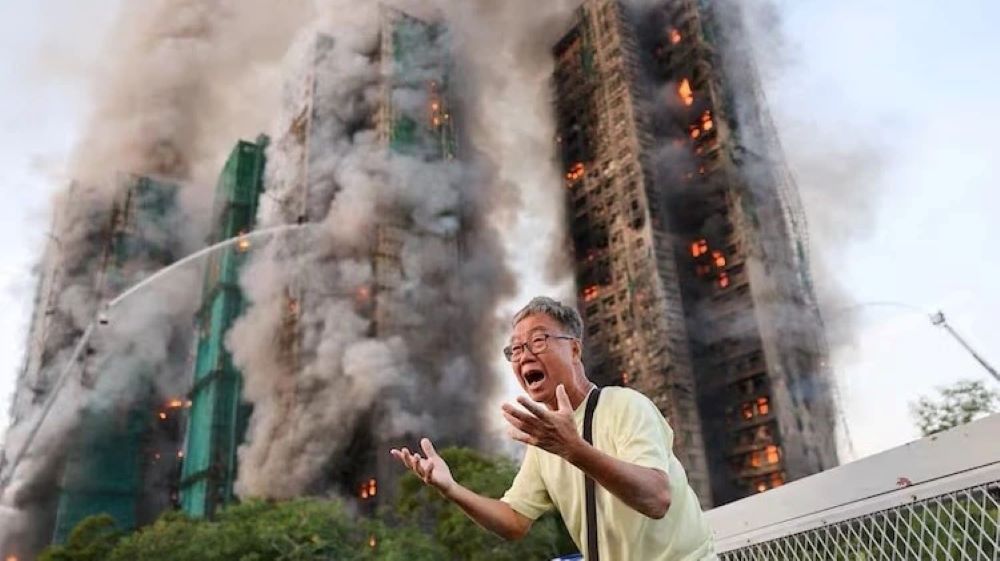 A man reacts, as smoke rises while flames engulf bamboo scaffolding across multiple buildings at Wang Fuk Court housing estate, in Tai Po, Hong Kong on November 26, 2025. Tyrone Siu/Reuters