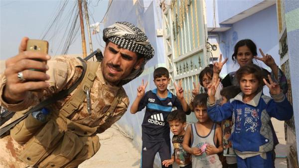 A Kurdish Peshmerga fighter takes a selfie with children after recapturing Fadiliya village