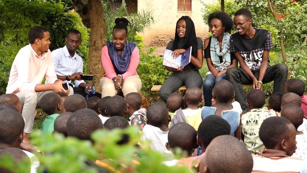 Dominique Uwase Alonga (centre right) reads a story to children at Ellie's Corner - a partner organization of Imagine We in Kigali.
