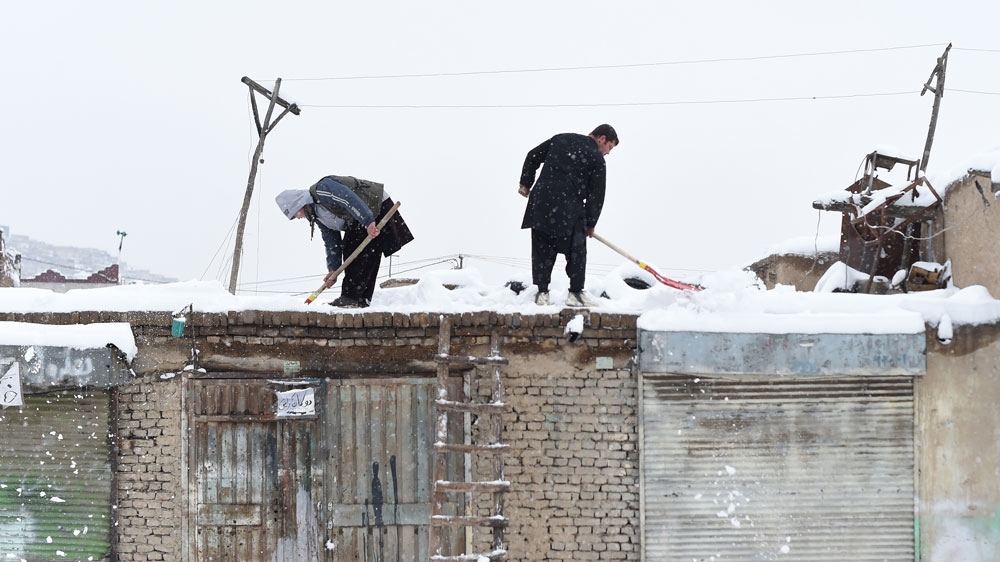 Afghan shopkeepers shovel snow from the roof of their shop during snowfall in Kabul
