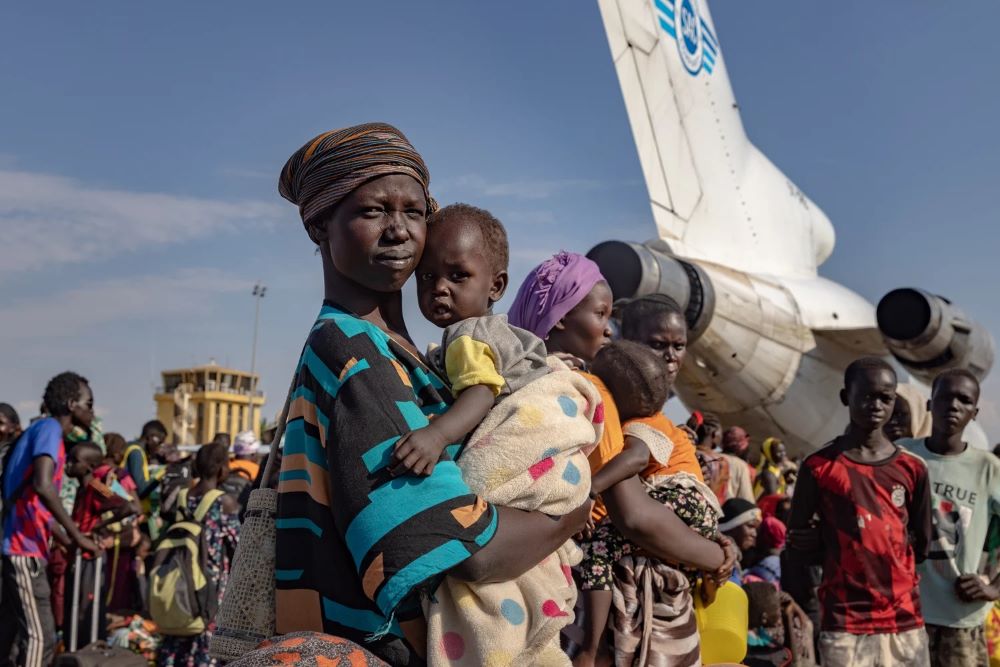 Achol Deng and her daughter wait with hundreds of South Sudanese returning refugees at Palouch Airport in South Sudan's Upper Nile State, after fleeing the conflict in Sudan.  © UNHCR/Andrew McConnell