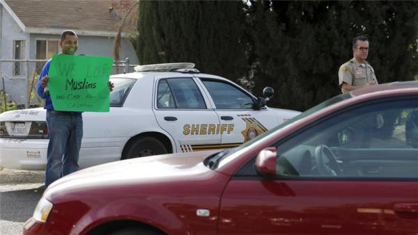 A man holds a sign saying 'We Love Muslims' after Friday prayers at a mosque where the shooting suspect was seen