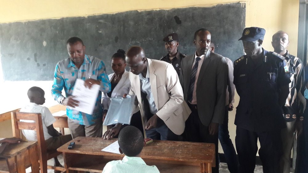 State Minister in charge of Primary and Secondary Education in the ministry of Education, Isaac Munyakazi (L) and other officials distributing examination papers to students including juveniles