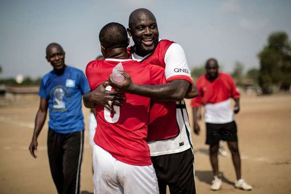 International Liberian soccer star, George Weah embraces a team member at the end of a match played on a dusty pitch at the Alpha Old Timers Sports Association in Paynesville in Monrovia on April 30, 2016.