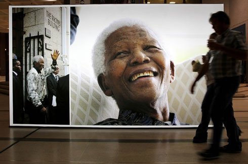 People walk on June 27, 2013 past a giant picture of former South African President Nelson Mandela at the Cape Town Civic Centre. South Africans have criticised a controversial painting that depicts the country’s president Jacob Zuma having sex with anti-apartheid leader Nelson Mandela.