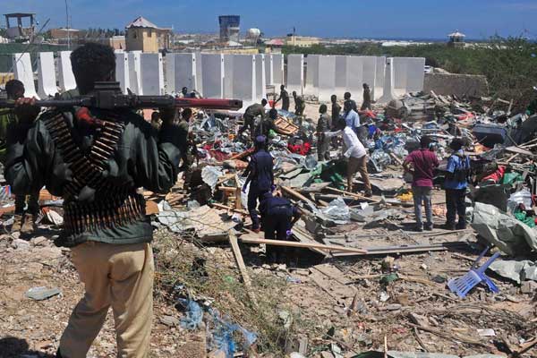 Civilians and soldiers stand amongst scattered objects at the scene of a car bomb attack near the Peace Hotel in Mogadishu on January 2, 2017. A car bomb killed at least 20 in Mogadishu on February 19, 2017.
