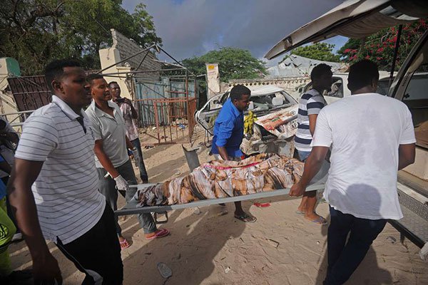 Volunteers carry a stretcher with a body bag from the site of an attack at the Pizza House restaurant in Mogadishu on June 15, 2017.