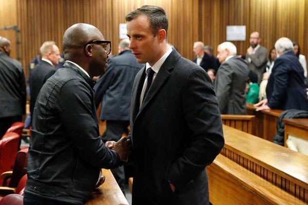 South African Paralympian athlete Oscar Pistorius (centre) speaks to a man at the High Court in Pretoria, on July 6, 2016 after being sentenced to six years in jail for murdering his girlfriend High Court in Pretoria three years ago.