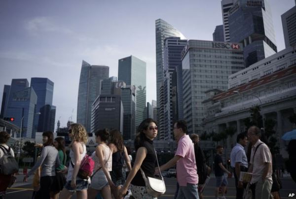 People walk across a main street in the financial district of Singapore.