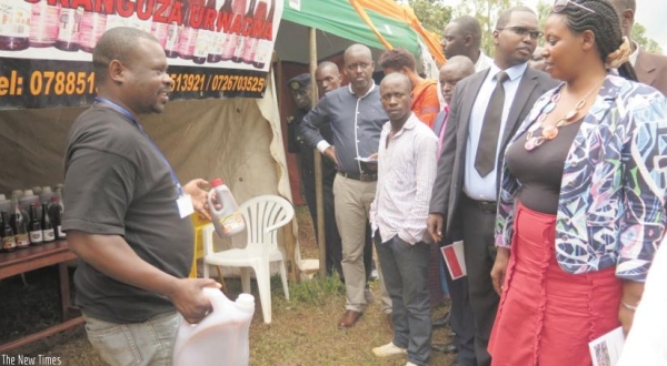 A banana wine maker showcases his products as the Southern Province executive secretary Izabiriza (R) and Jean Bosco Bigirimana, the PSF president in the Southern Province (2nd R), visit his stand on Monday.