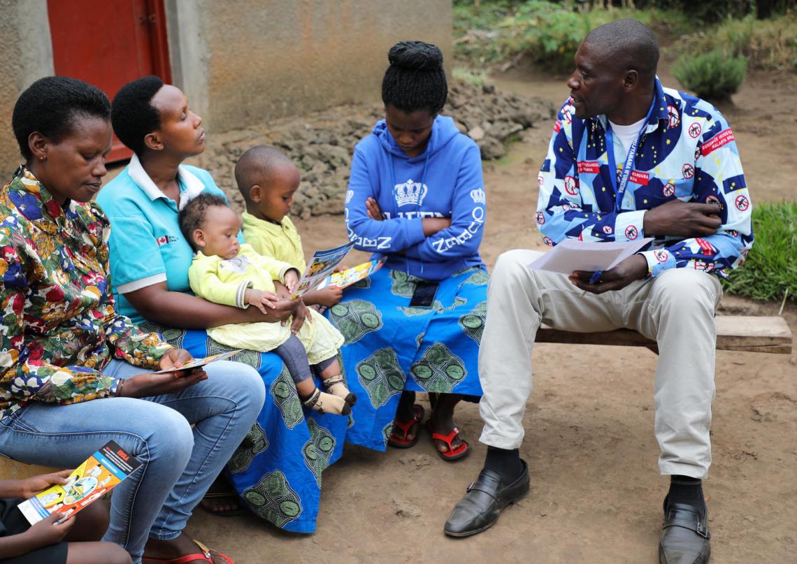 Daniel sits with a family outside their home as he discusses symptoms and prevention measures of Ebola.