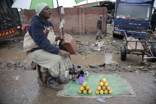 A woman with baby strapped to her back sells mangoes laid out on a mat around wet and dirty conditions in Mbare, Harare, Zimbabwe, January 17, 2017. Heavy rains have deluged Zimbabwe in recent days, causing floods and killing people who attempted to cross rivers that had burst their banks.